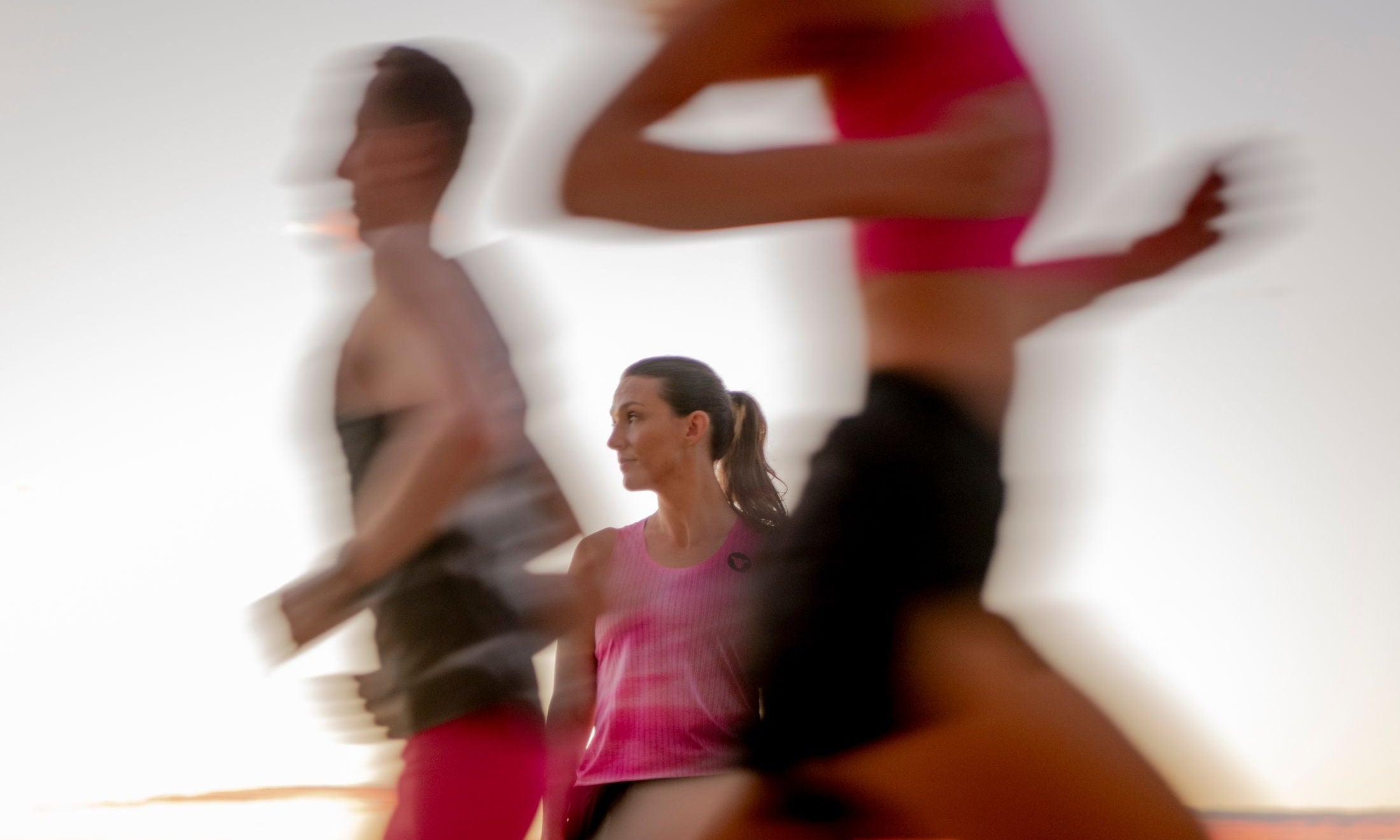 A runner stands still in focus while training partners blur past at sunrise